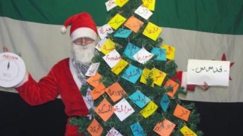 Syrian Santa with the Syrian Christmas tree that has all the cities and towns of Syria on it. Source: facebook.