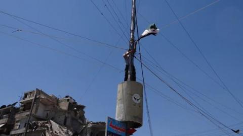 أحد النشطاء يتحدى الإسلاميين و يرفع علم الثورة بدلا من العلم في دوار الحلوانية في حلب. المصدر: الصفحة الرسمية للحملة
