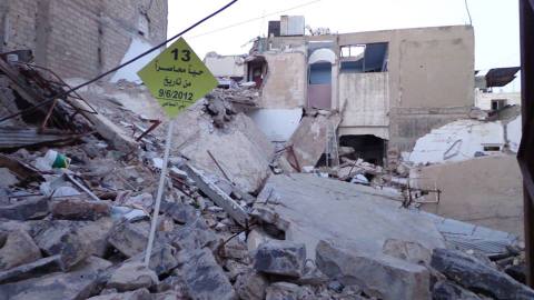 شعار للحملة في حي بني السباعي المحاصر وخلفه الدمار. المصدر: الصفحة الرسمية للحملة على الفيسبوك