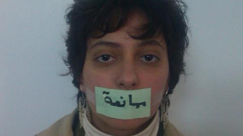 رزان غزاوي وهي تضع على فمها شريط لاصق مكتوب عليه ممانعة كدلالة على أن النظام الذي يقدم نفسه يقيد الحريات. المصدر: الصفحة الشخصية لرزان غزاوي على الفيسبوك