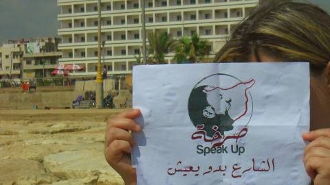 لافتة رفعتها إحدى الناشطات بعد أن غطت وجهها في مدينة طرطوس الساحلية. المصدر: الصفحة الرسمية للمجموعة على الفيسبوك