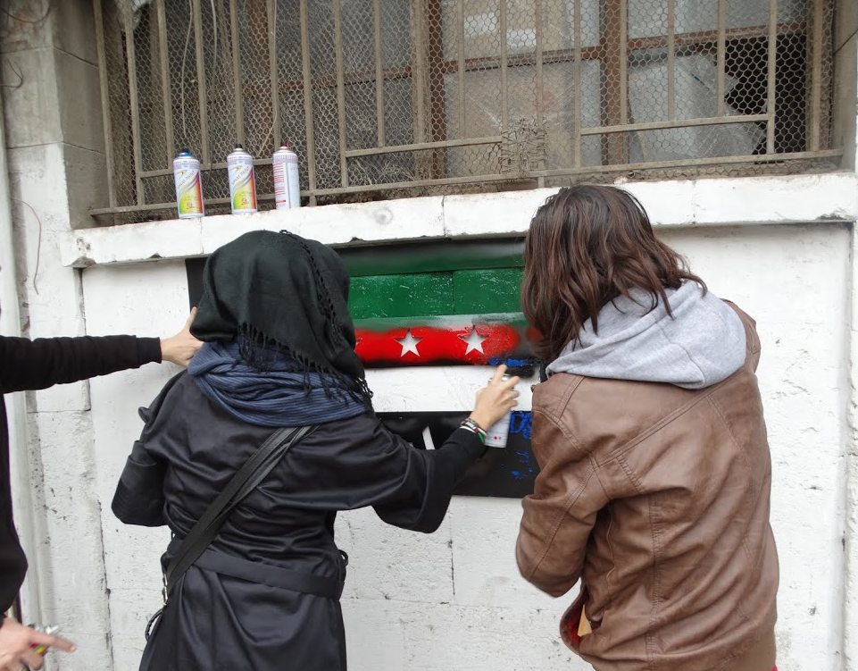 ناشطتان تقومان ببخ العلم على أحد جدران مدينة حلب. المصدر: مؤسسة اليوم التالي