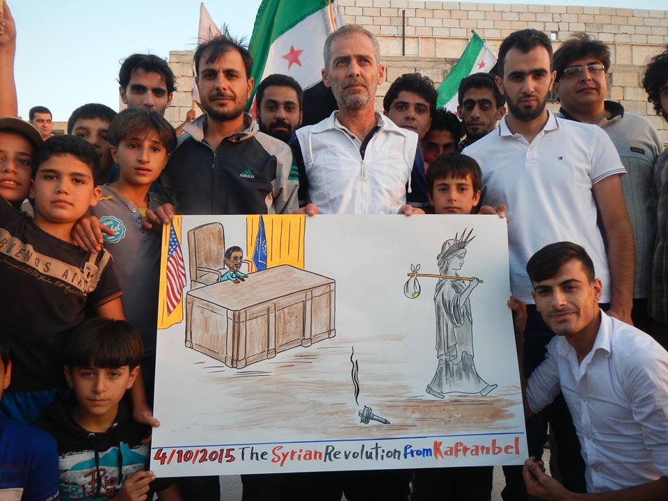 متظاهرون في كفرنبل يرفعون كاريكاتيرا يسخر من الموقف الأمريكي في سوريا بعد التدخل الروسي. المصدر: صفحة الناشط رائد الفارس على الفيسبوك