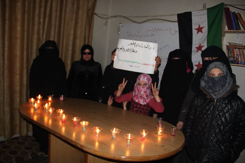 نساء التجمع يرفعن لافتة ويشعلن الشموع.المصدر: الصفحة الرسمية للتجمع على الفيسبوك