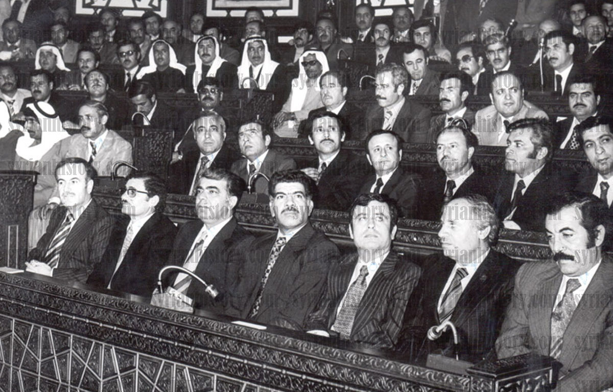[Photo: Hafez al-Asad's first inauguration as President in the People's Council, March 1971. L–R: Asad, Abdullah al-Ahmar, Prime Minister Abdul Rahman Khleifawi, Assistant Regional Secretary Mohamad Jaber Bajbouj, Foreign Minister Abdul Halim Khaddam and People's Council Speaker Fihmi al-Yusufi. In the third civilian row are Defense Minister Mustafa Tlass (MP in the 1971 Parliament) and Air Force Commander Naji Jamil. Behind Tlass is Rifaat al-Assad, Assad's younger brother. On the far right in the fourth row is future vice president Zuhair Masharqa, and behind Abdullah al-Ahmar is Deputy Prime Minister Mohammad Haidar - Damascus (Syrian History Archive/Public Domain via Wikimedia Creative Commons)].
