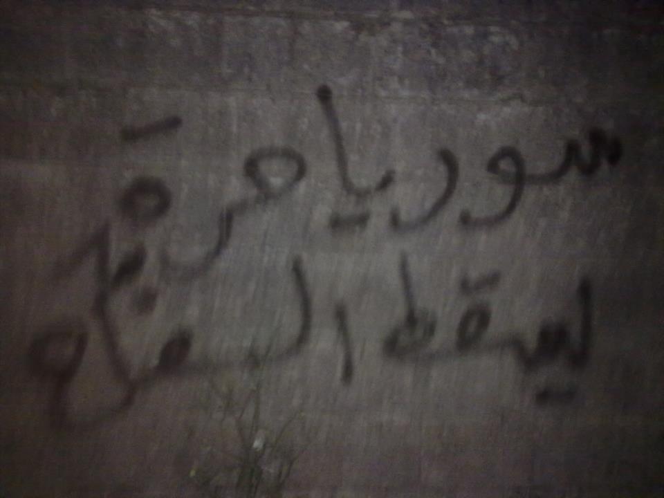 [Photo: A slogan written by Ayman in rural Jablah. It reads “Free Syria, Down with the Butcher” (SyriaUntold)].