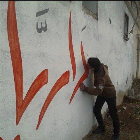 مواطن من مدينة داريا يقبل اسم مدينته المكتوب على الجدار قبل رحيله عنها. المصدر: المجلس المحلي لمدينة داريا)