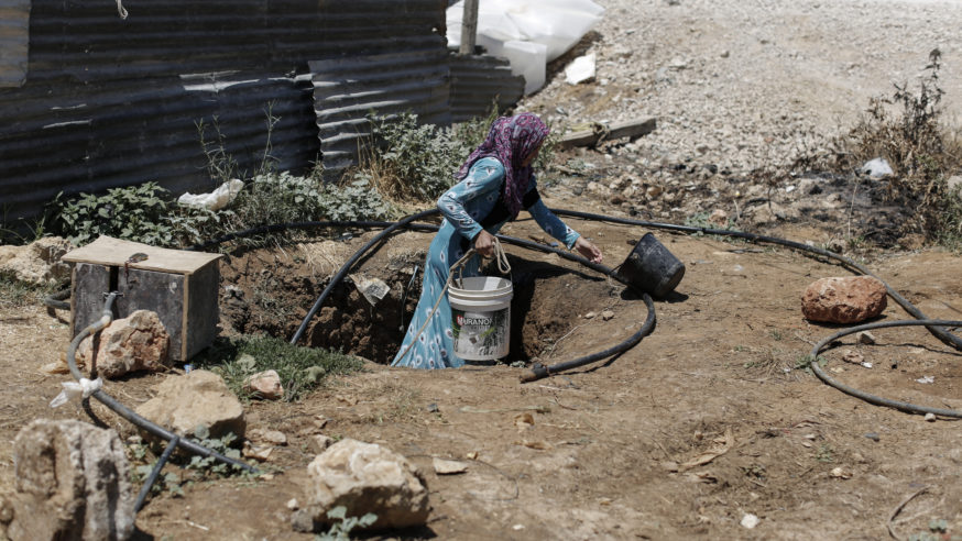 روعة، 21 عاما، أم لثلاثة أطفال من حلب، تسحب ماء من بئر في مخيم عشوائي للاجئين السوريين بوادي البقاع. البئر هو مصدر الماء الوحيد في المخيم وهو غير صالح للشرب. أخبر بعض السكان مجلس اللاجئين النرويجي أن من يشرب من البئر بشكل دائم يعاني من أمراض جلدية وآفات اخرى – لبنان – 24/7/2014 (سام تارلينغ/ مجلس اللاجئين النرويجي عبر CC BY-ND 2.0 )].